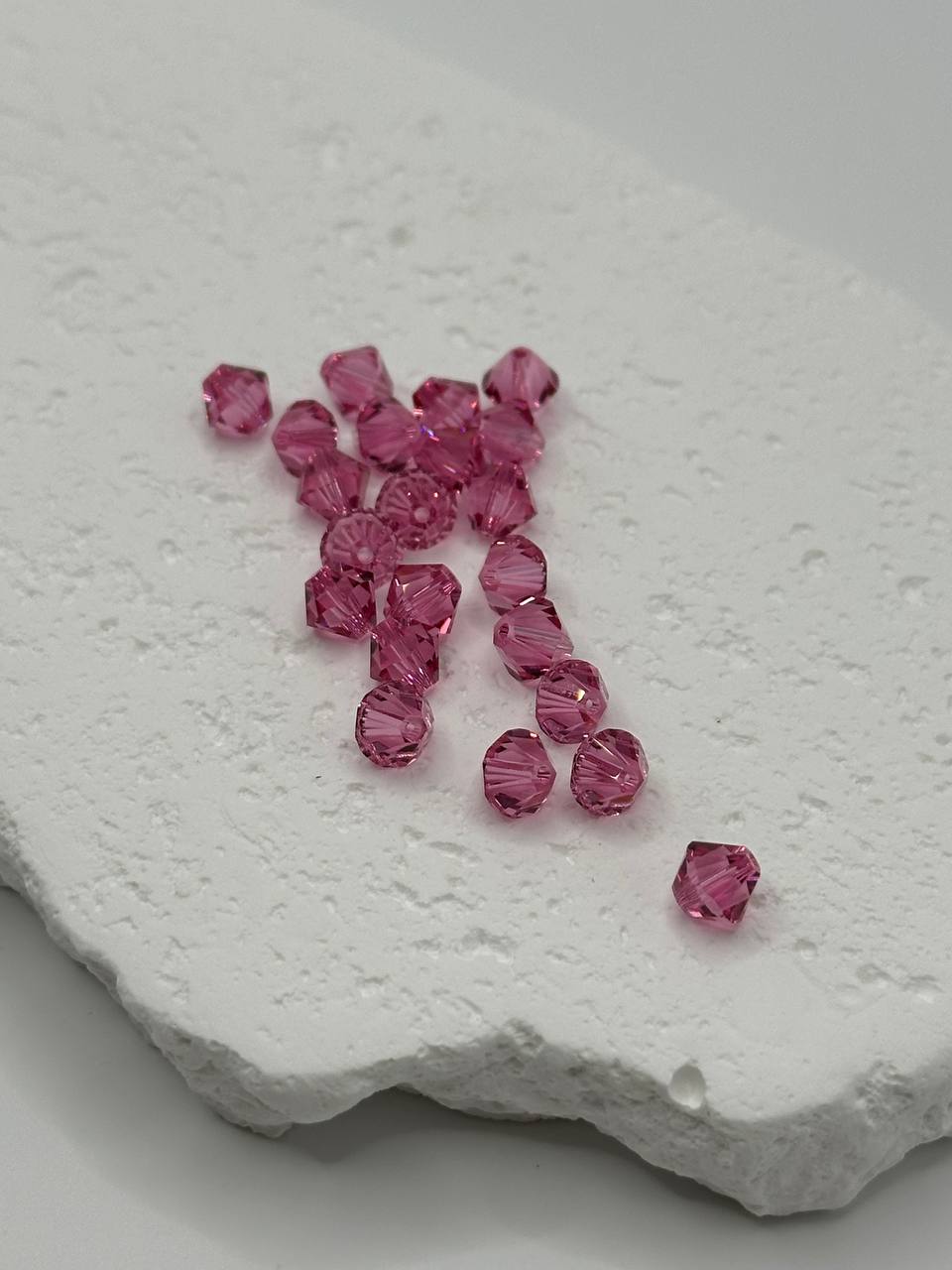 Pink crystal bicone beads on a textured white surface