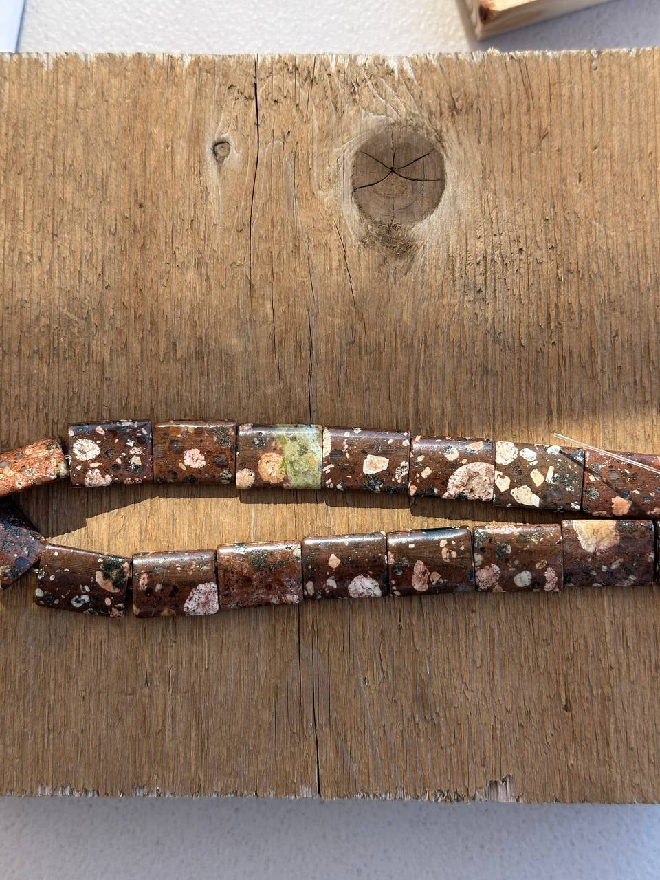 Brown, creamy, green rhyolite puffed rectangle beads on wooden surface