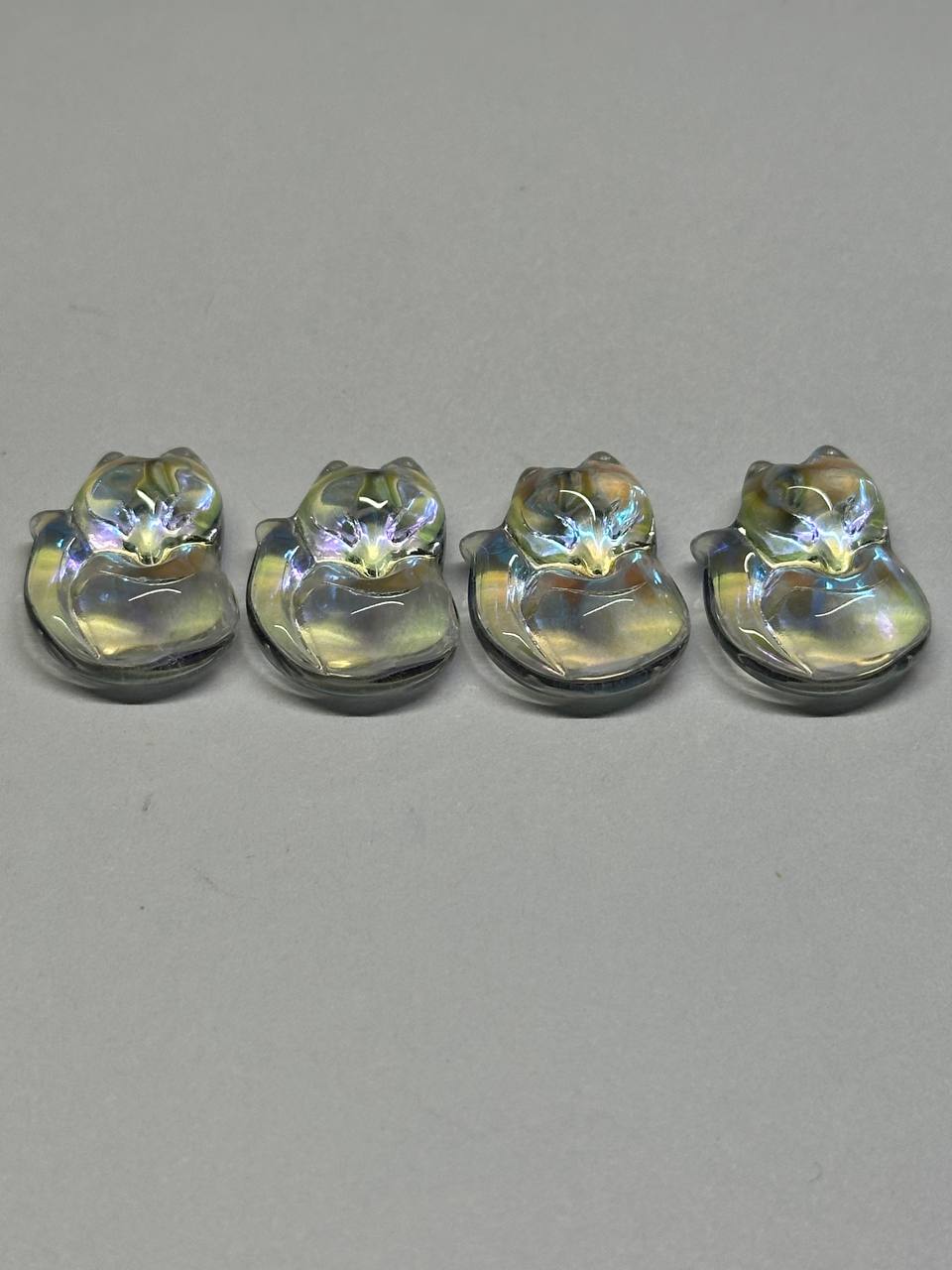 Four glass foxes with iridescent finish on a gray background