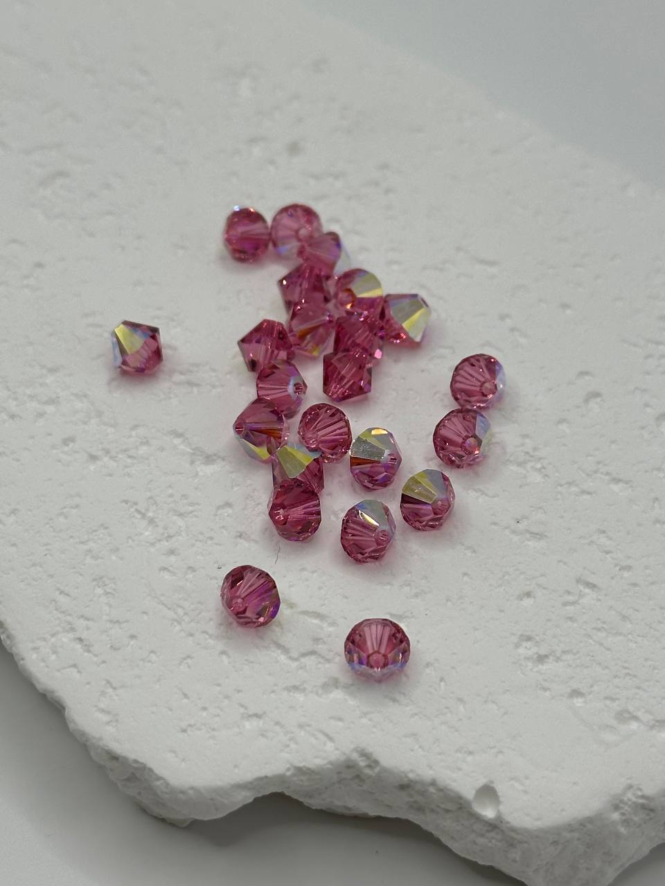 Pink beads with a metallic sheen on a textured white surface