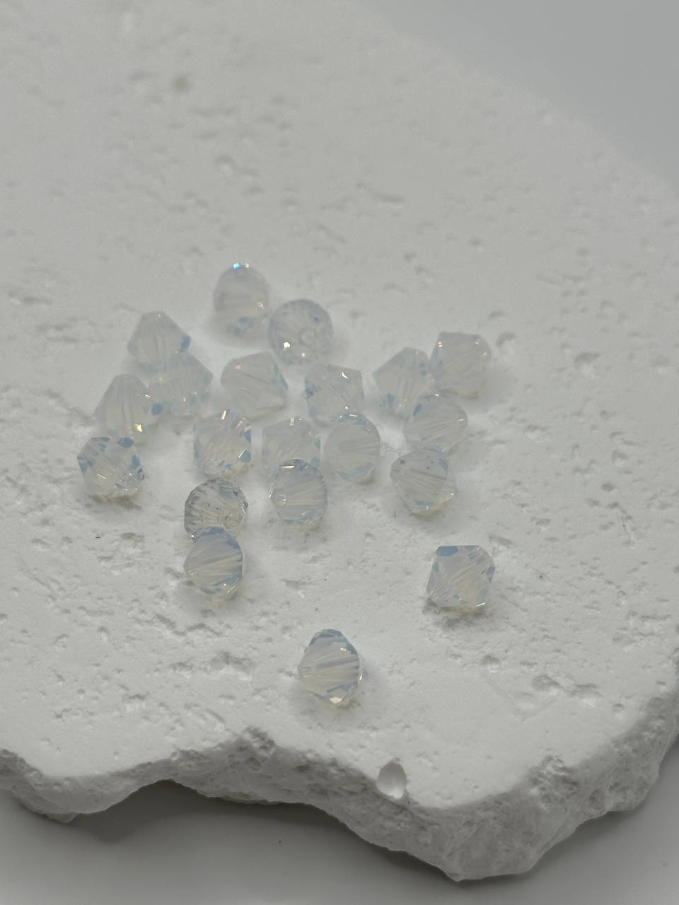 White opal crystal bicone beads with a metallic sheen on a textured white surface
