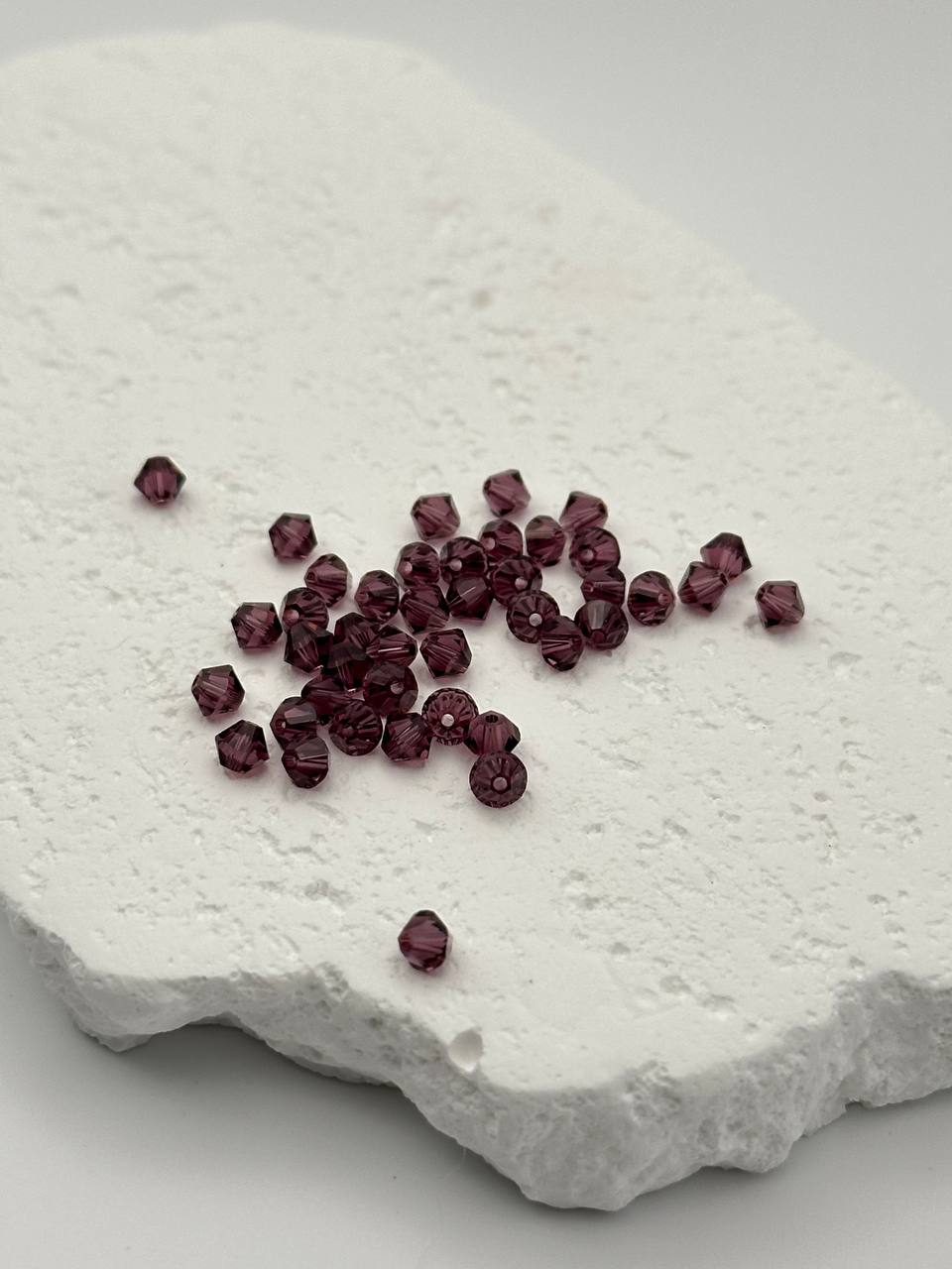 Amethyst bicone beads on a textured white surface