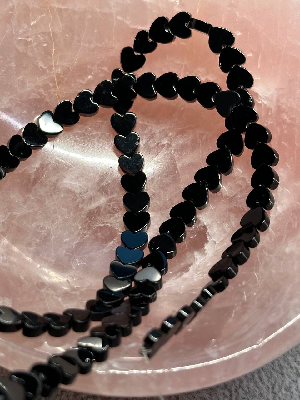 Black heart-shaped beads on a pink textured surface