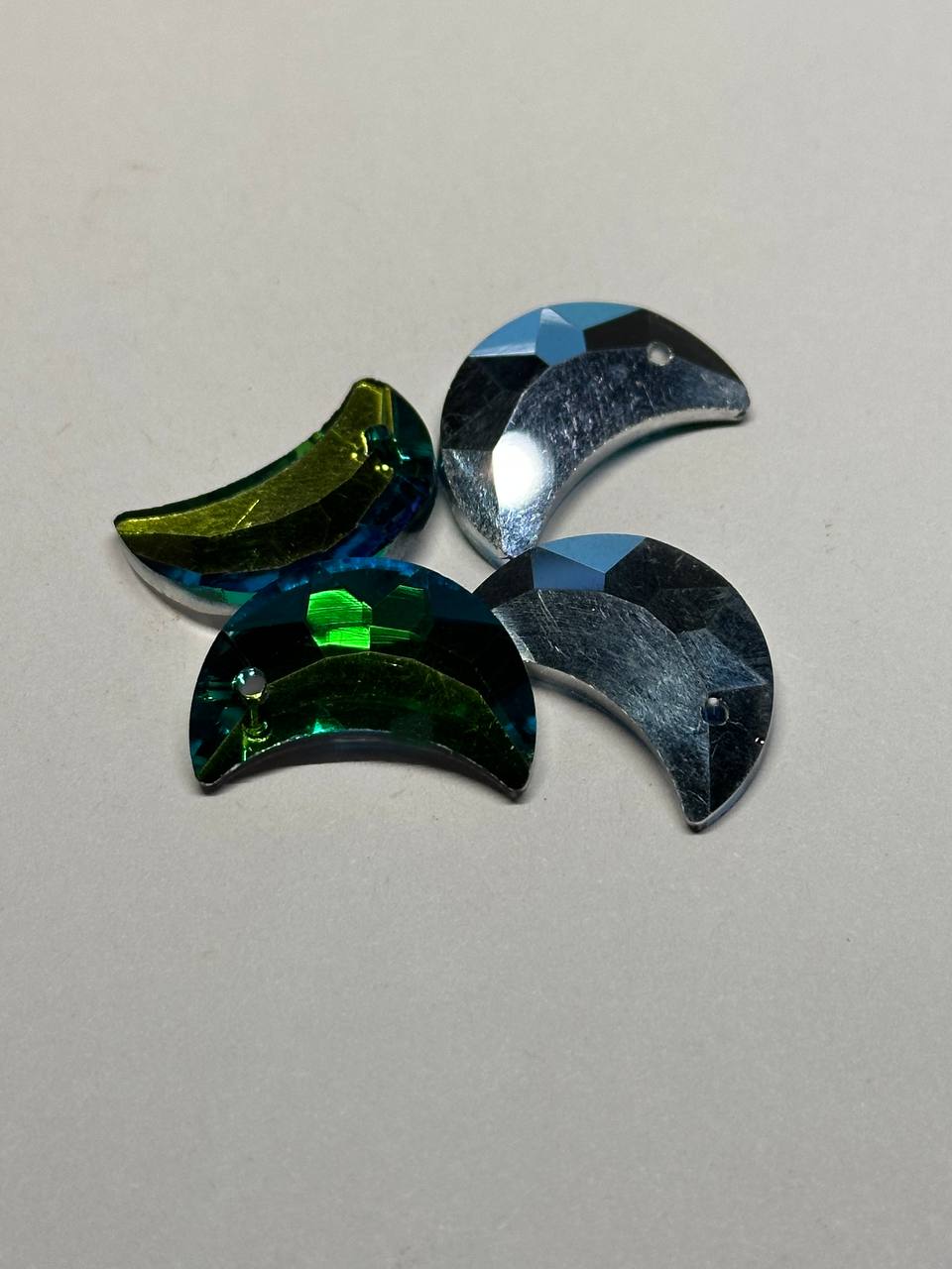 Four green and blue crescent-shaped beads on a light gray background