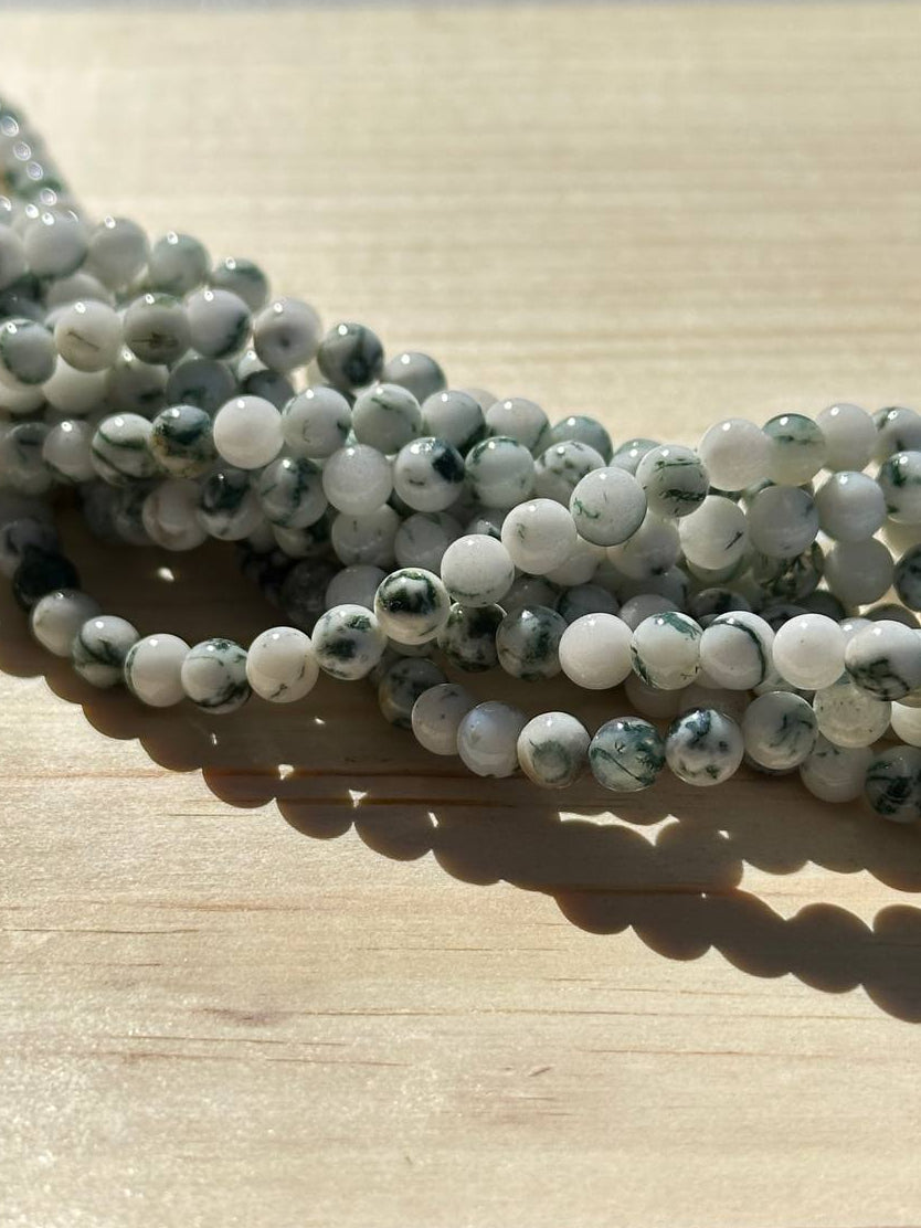 Green and white tree agate beads on a wooden surface