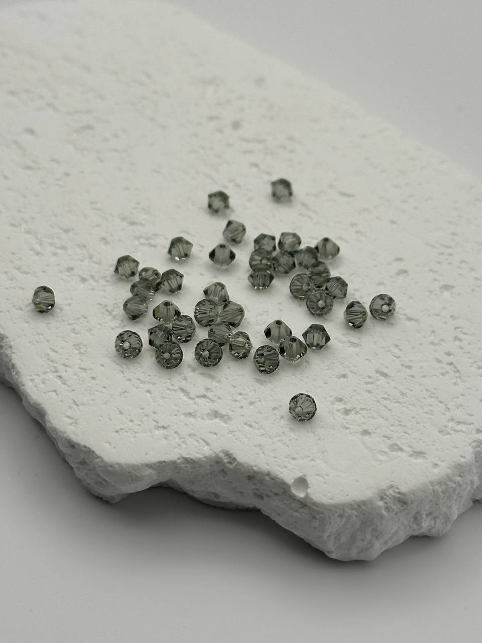 Small black diamond bicone beads on a textured white stone surface