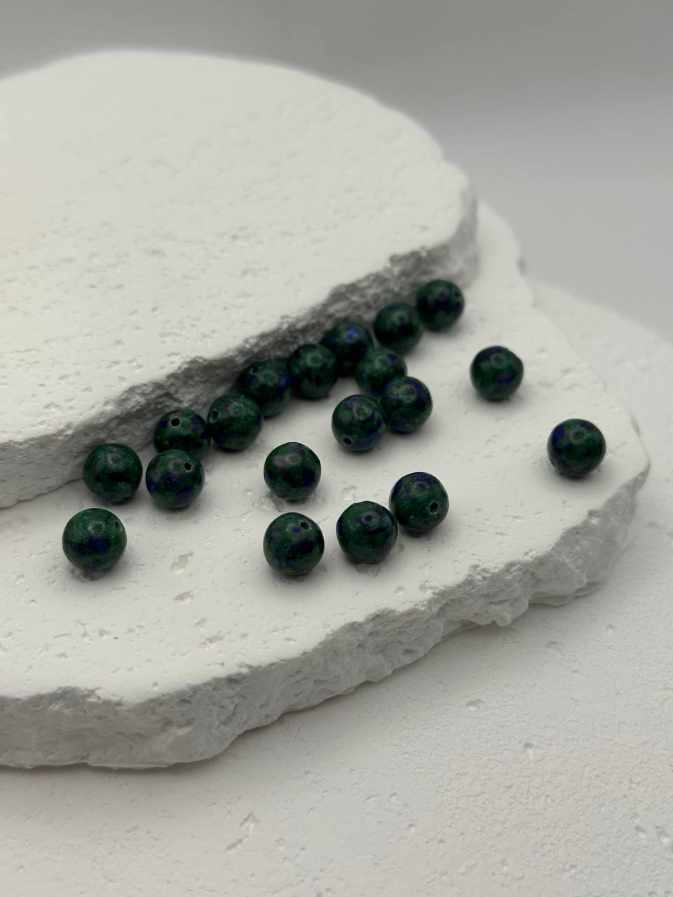 Green beads on a textured white stone surface