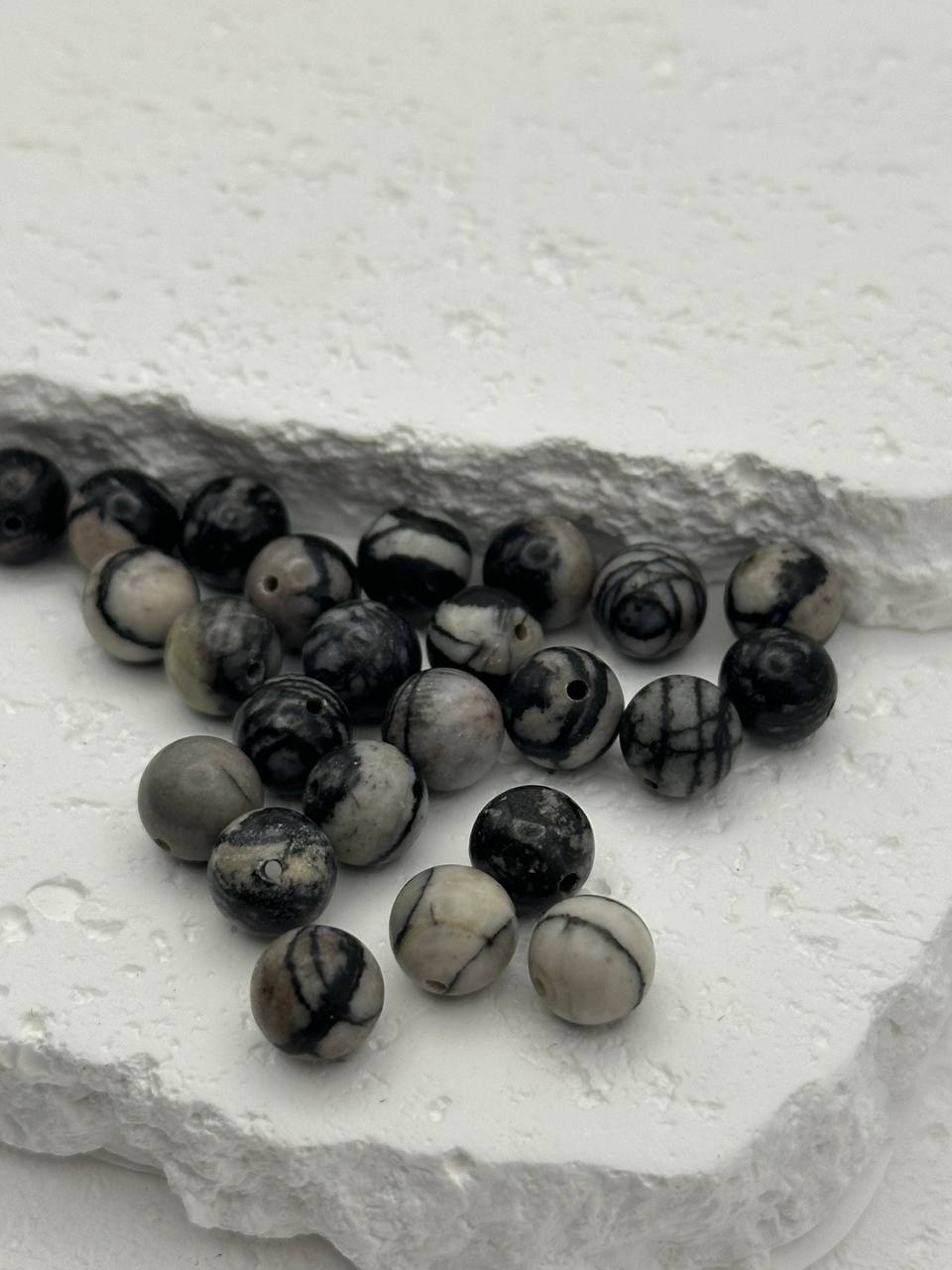 Black and white marbled beads on a textured stone surface