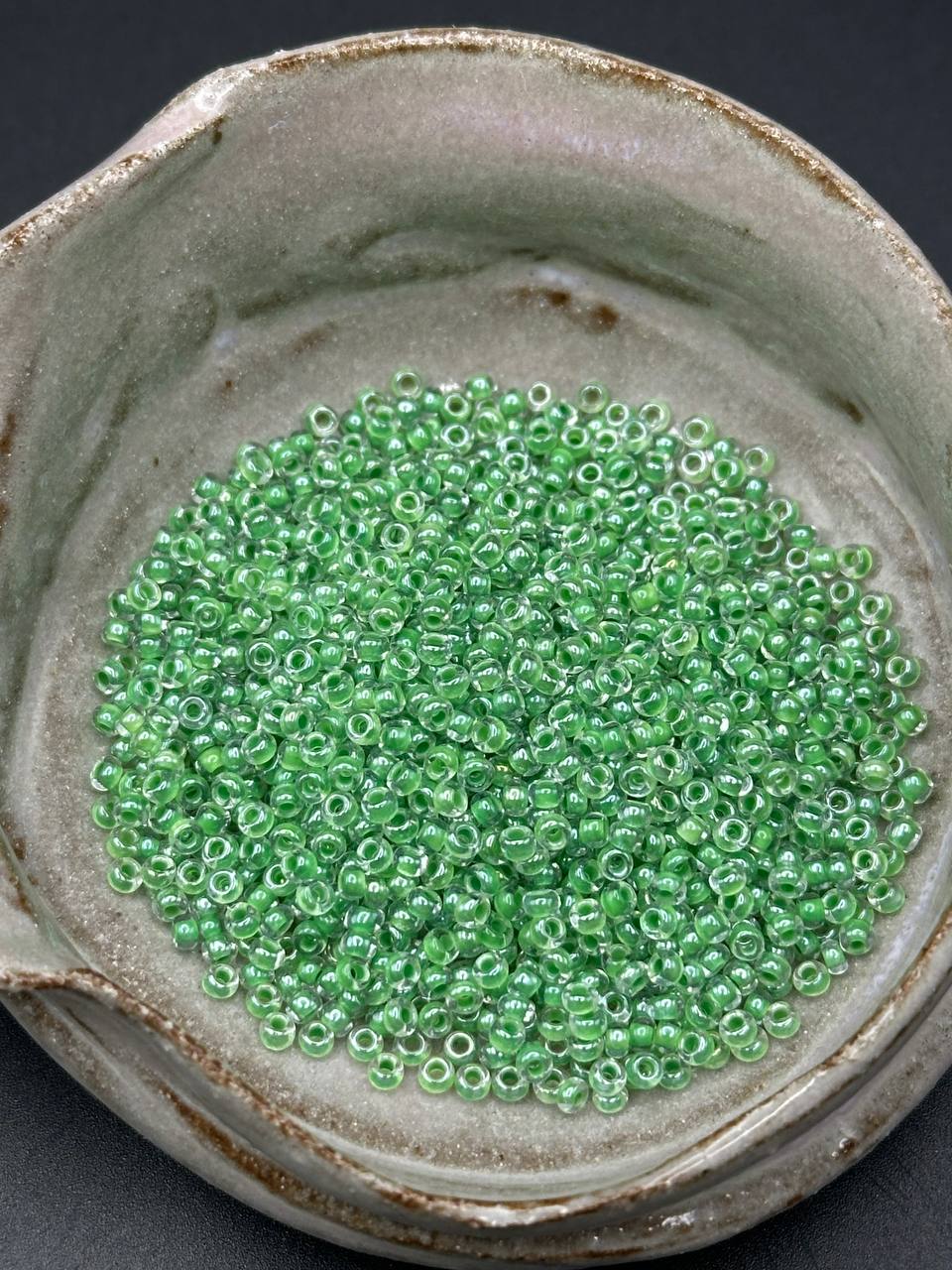 Green beads in a ceramic container on a dark background