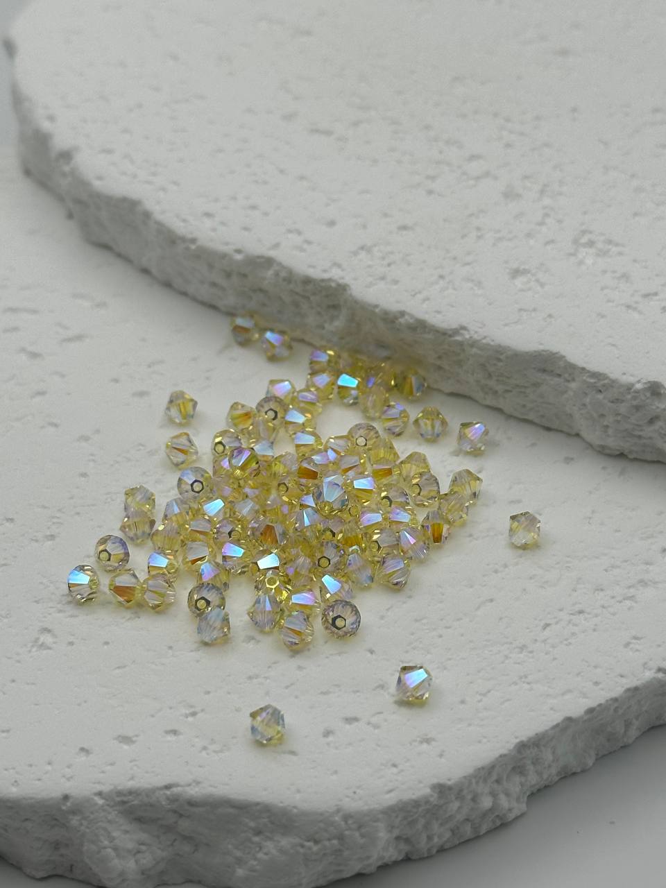 Small jonquil bicone beads with a metallic sheen on a stone surface