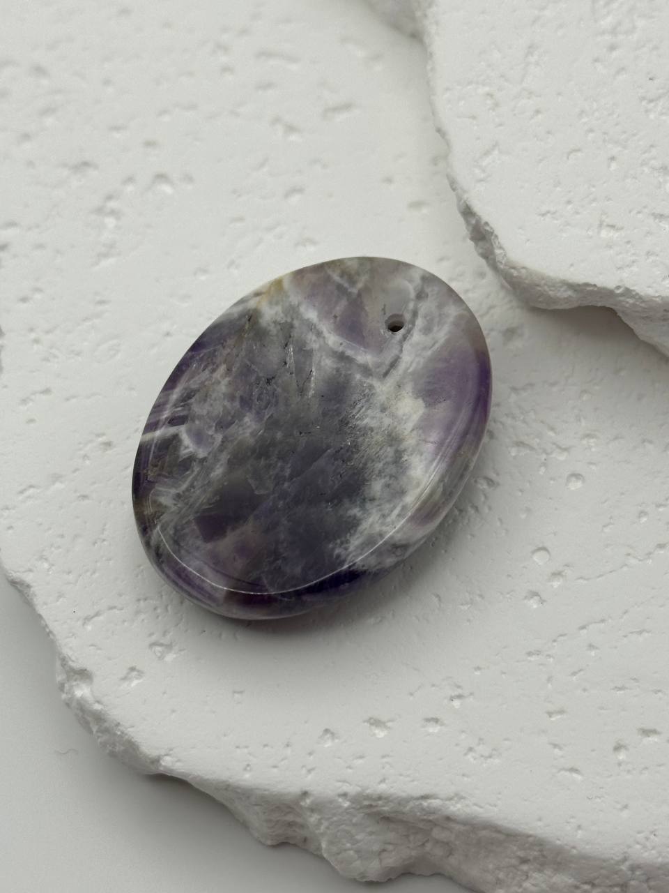 Purple stone with a hole on a textured white surface