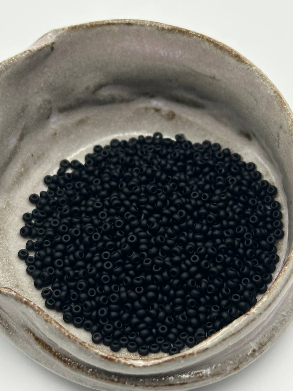 Close-up of black beads in a ceramic container on a white background