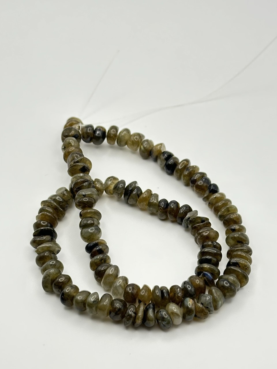 A string of irregular rondelle labradorite inclusion smoky quartz beads on a white surface