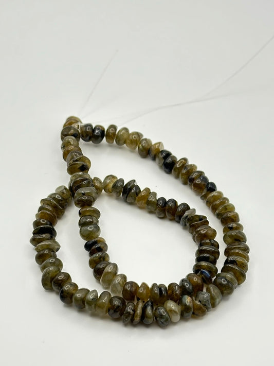 A string of irregular rondelle labradorite inclusion smoky quartz beads on a white surface