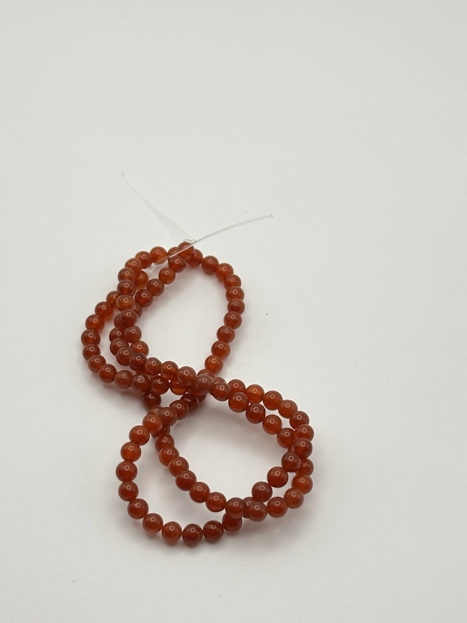 A string of bright reddish orange carnelian agate beads on a white surface