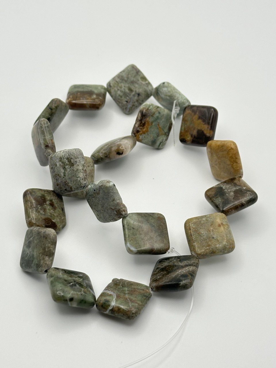String of green and brown rhyolite beads on a white background