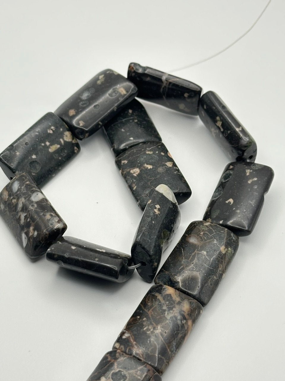 A string of rectangle basalt beads on a white surface 