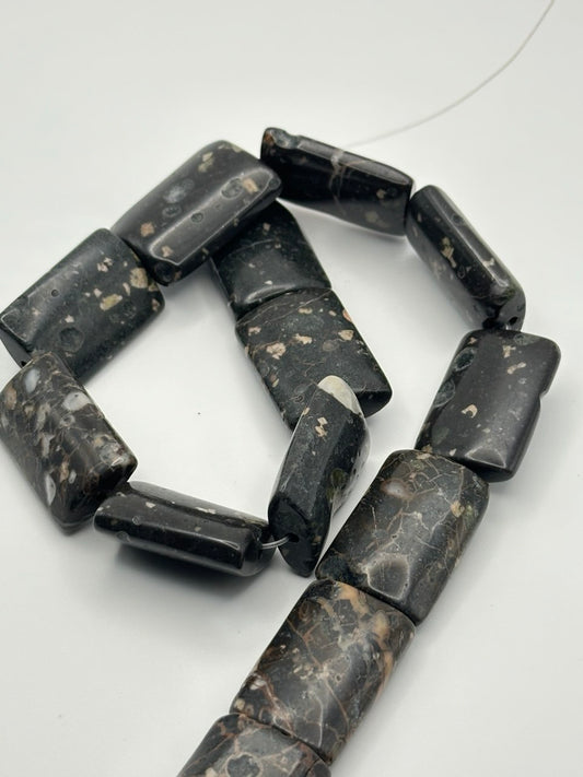 A string of rectangle basalt beads on a white surface 