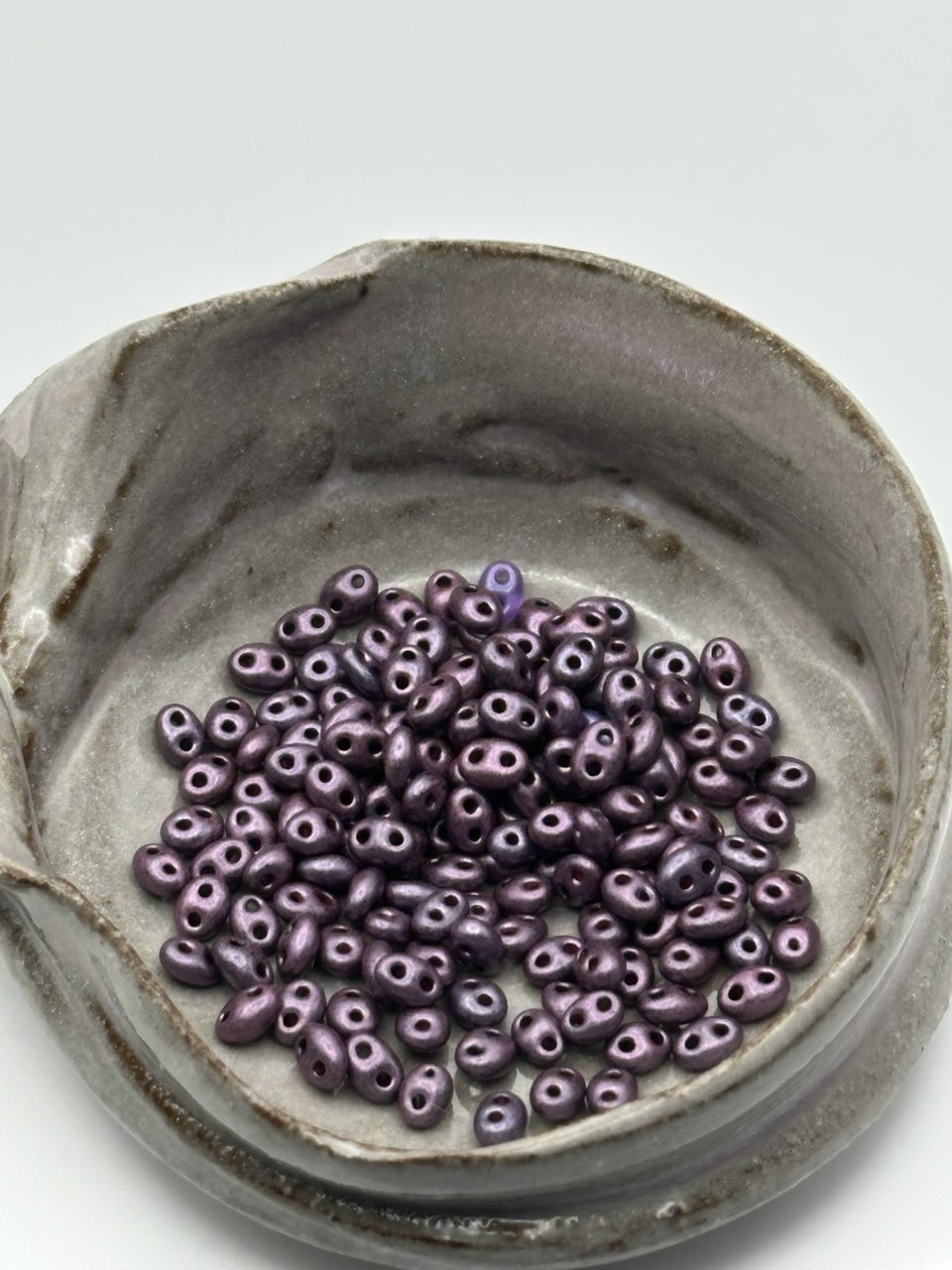 Purple superduo beads in a ceramic dish on a light gray background