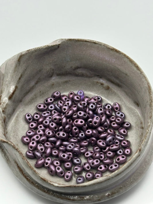 Purple superduo beads in a ceramic dish on a light gray background
