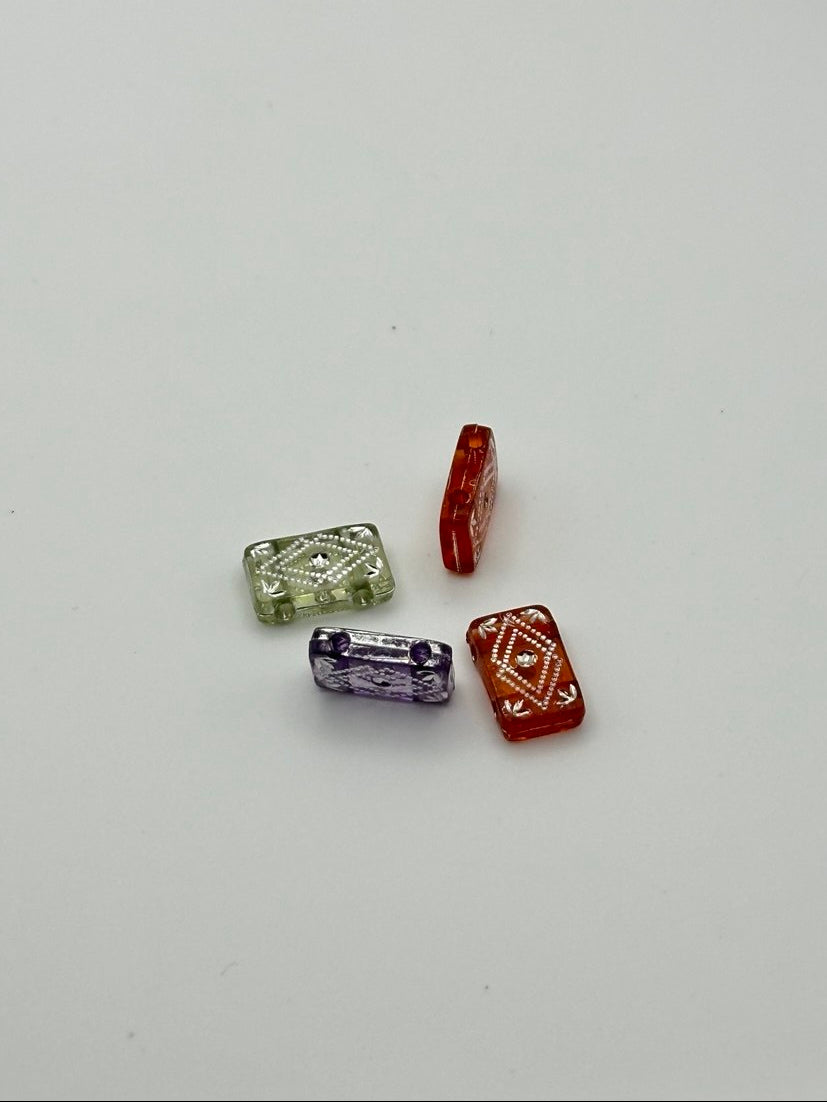 Four rectangular beads in green, purple, red, and brown on a light gray background