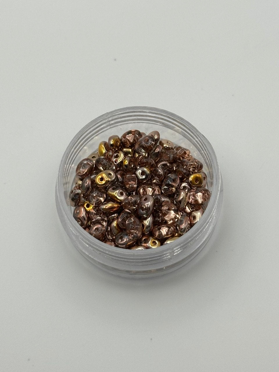 Small clear container filled with small metallic superduo beads on a light gray background