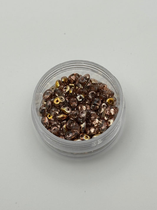 Small clear container filled with small metallic superduo beads on a light gray background