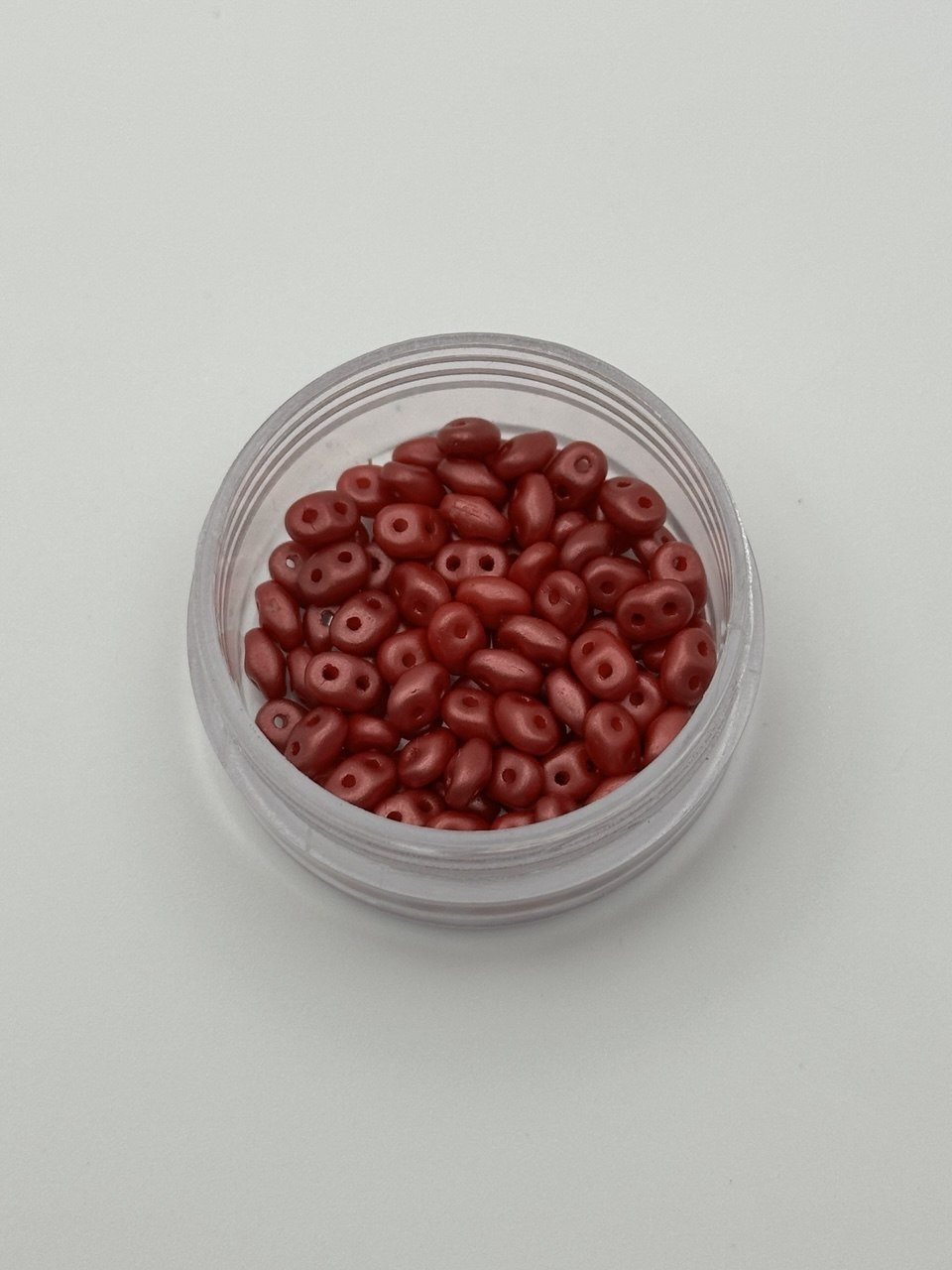 Small clear container filled with red beads on a light gray background