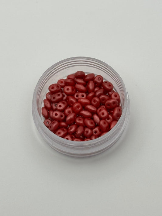 Small clear container filled with red beads on a light gray background