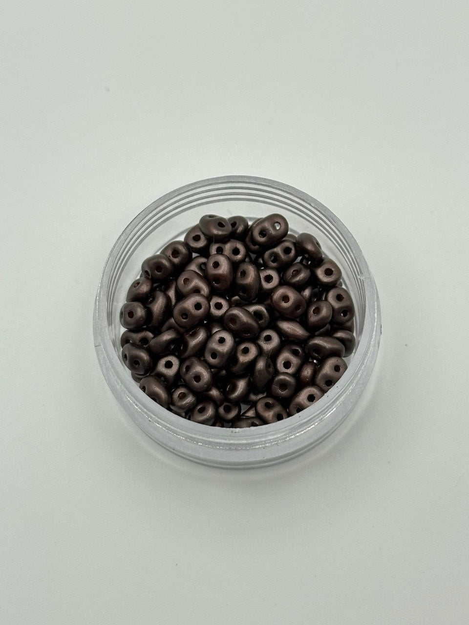Small clear container filled with dark brown beads on a light gray background