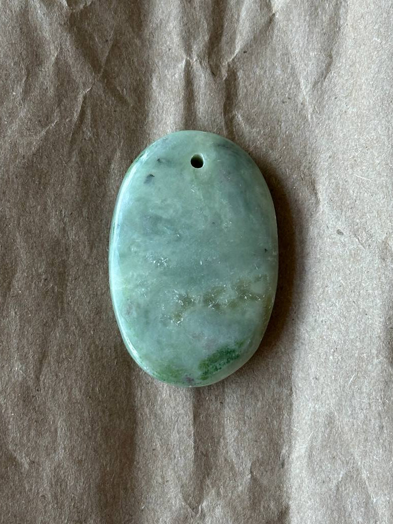 An oval jadeite cabochon on a brown paper background