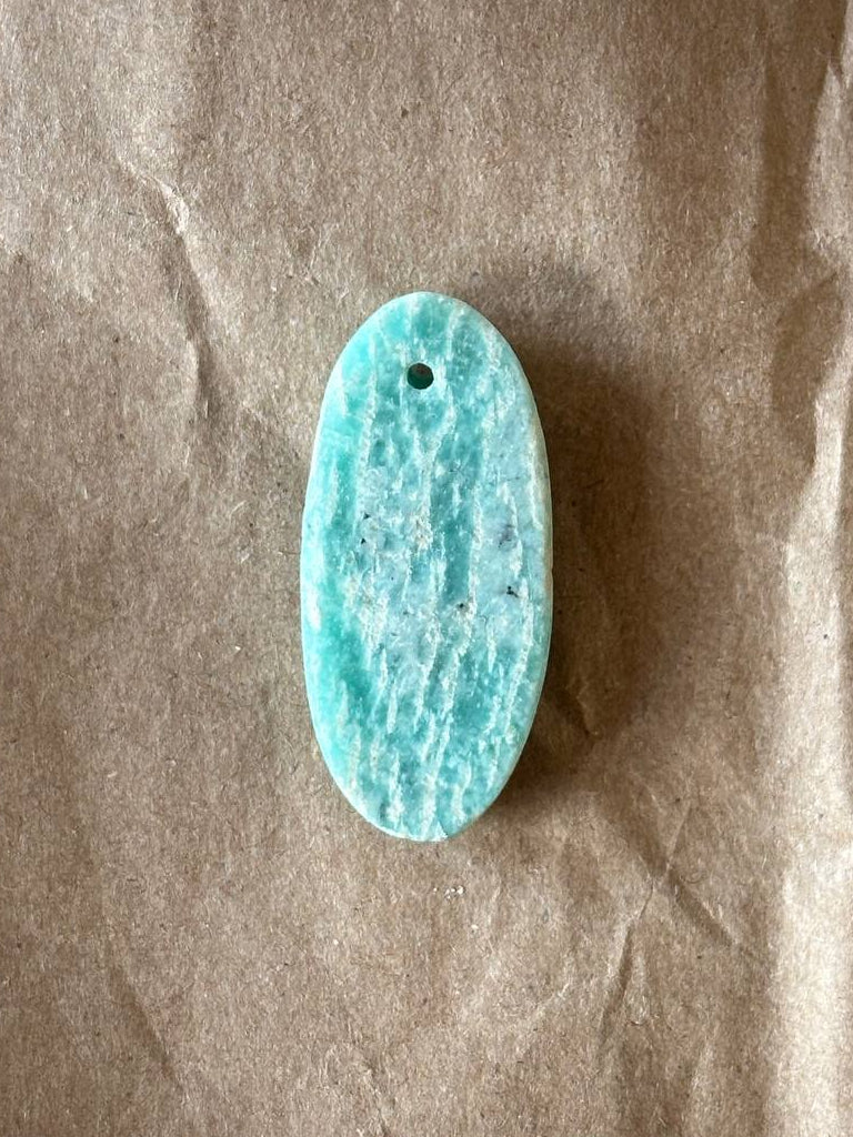 Amazonite oval cabochon with inclusions on brown paper background