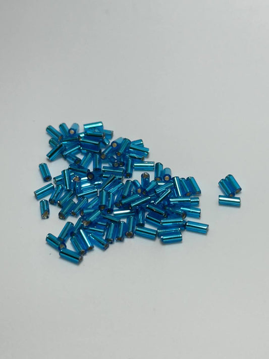 A small pile of blue silver lined bugle beads on white background