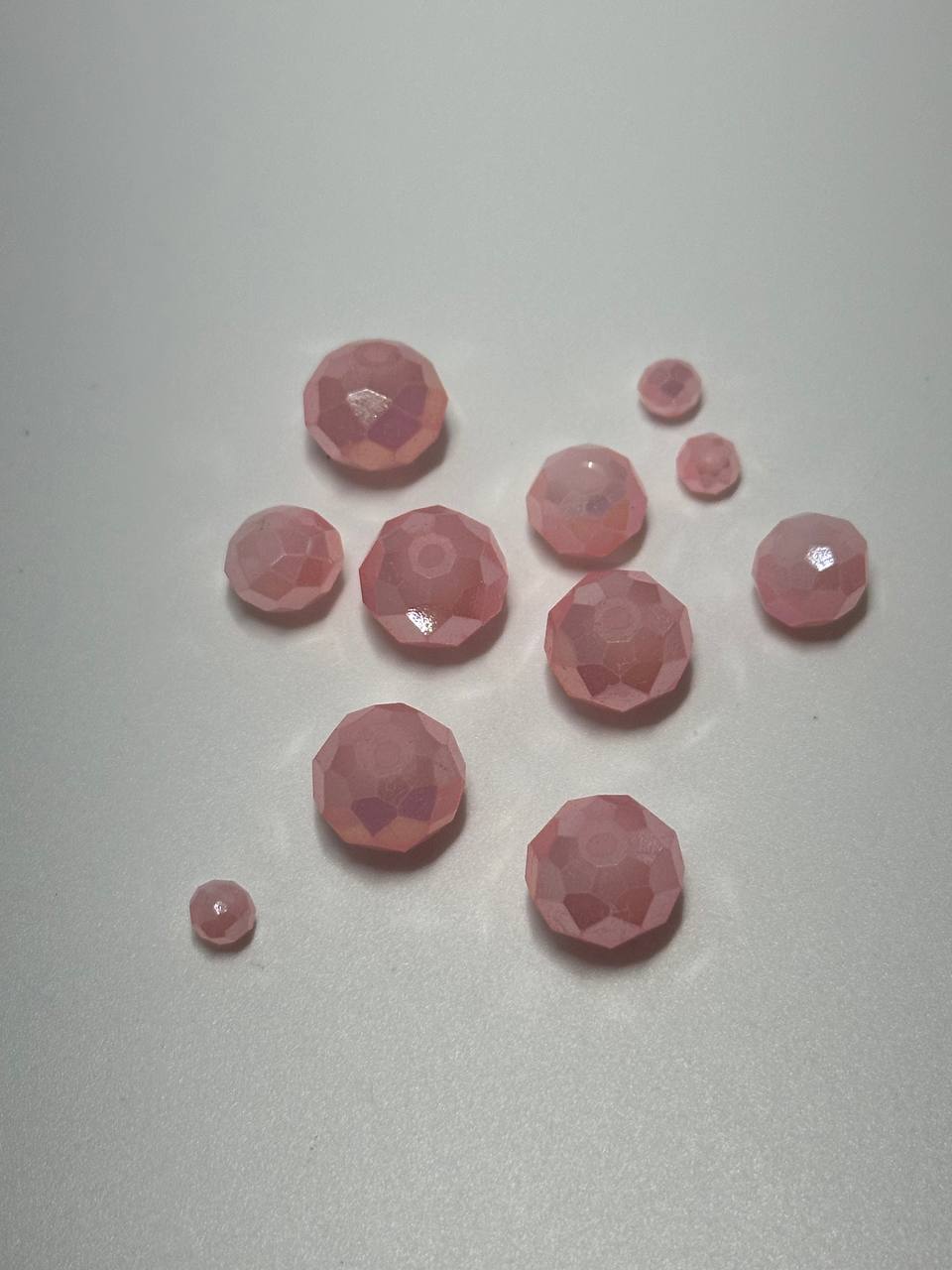 A small pile of rose AB faceted rondelle beads on white surface