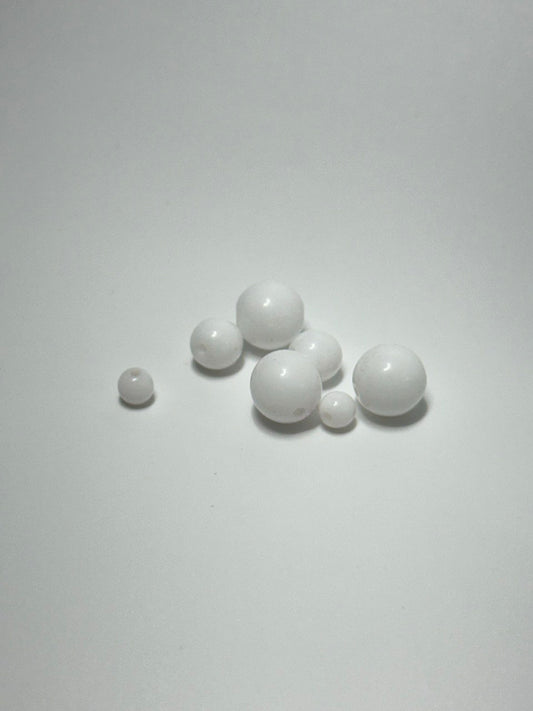 Six white spherical beads of varying sizes with a single hole, arranged on a plain light gray background.