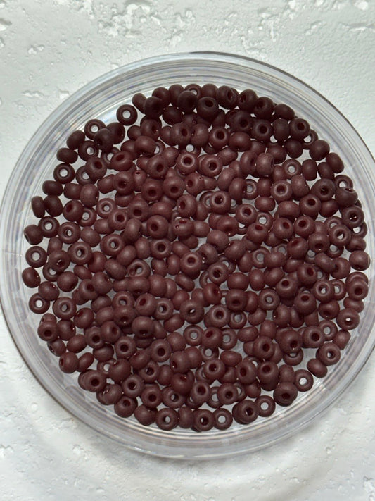A small pile of toho size 6 opaque chocolate dark brown oxblood seed beads on white surface