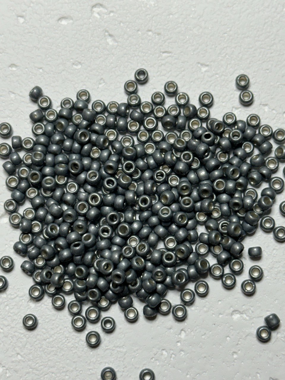 a small pile of permafinish steel sage 8/0 toho beads on white surface
