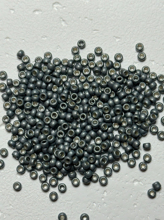 a small pile of permafinish steel sage 8/0 toho beads on white surface