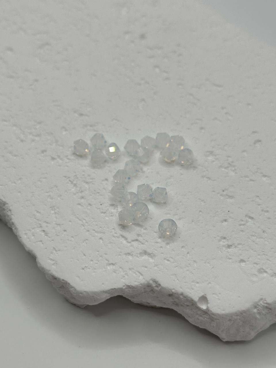 Small white opal crystal bicone beads on a textured white surface