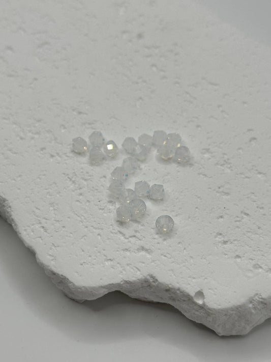 Small white opal crystal bicone beads on a textured white surface