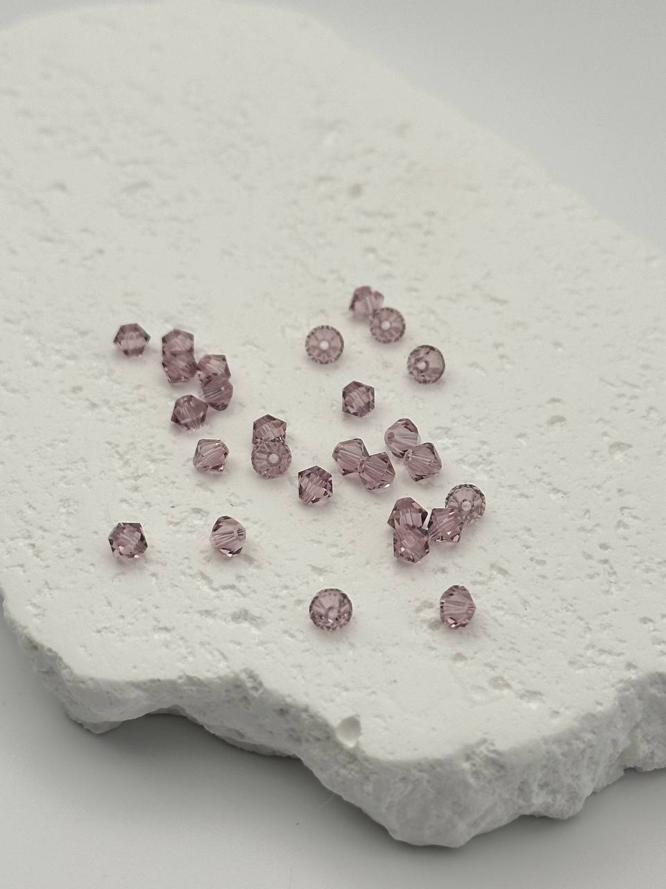 Light amethyst bicone beads on textured surface