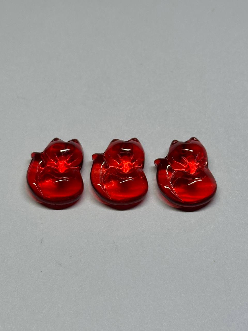 Three red glass fox-shaped beads on a gray background