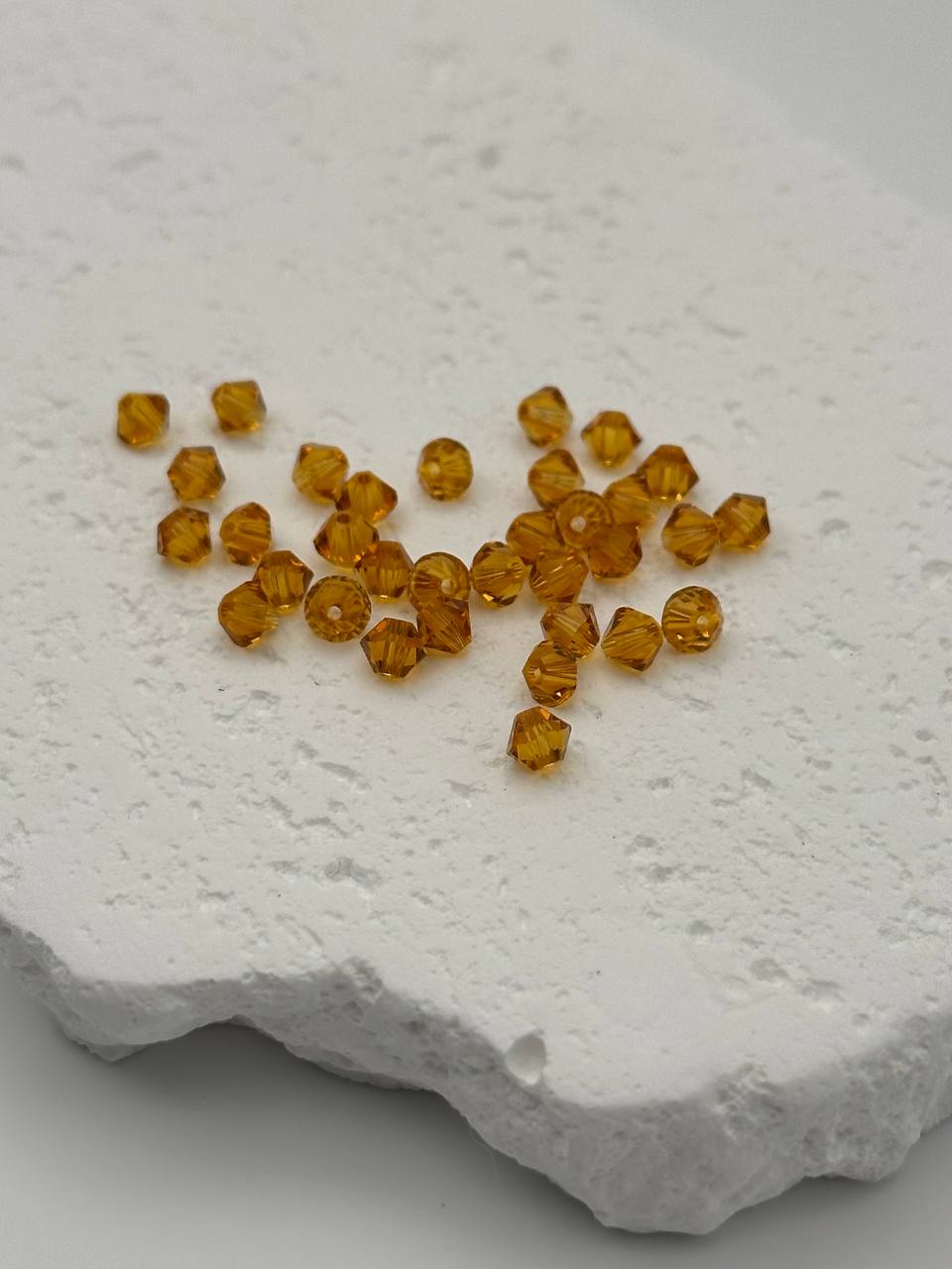 Small amber-colored bicone beads on a textured white surface