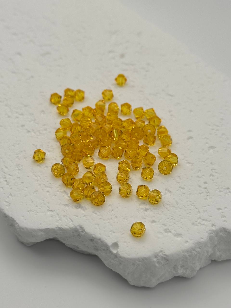 Yellow bicone beads scattered on a textured white surface