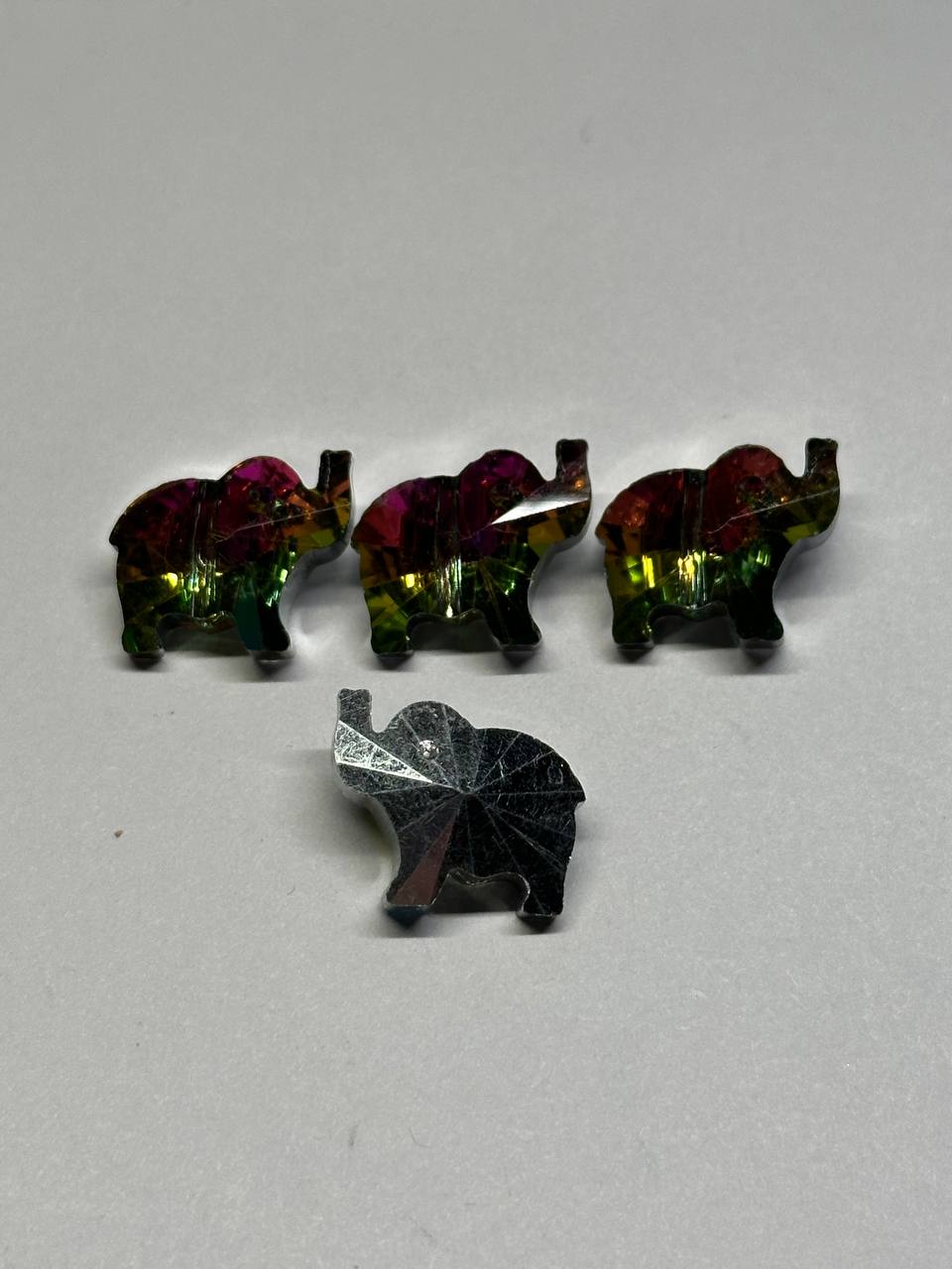 Four multicolored elephant shaped beads on a gray background