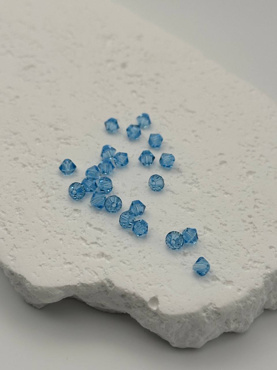 Blue bicone beads scattered on a textured white surface