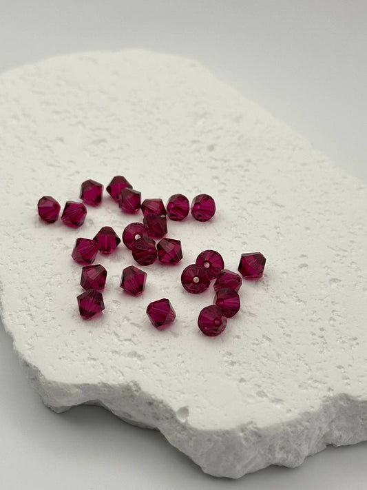 Ruby bicone beads on a textured white surface