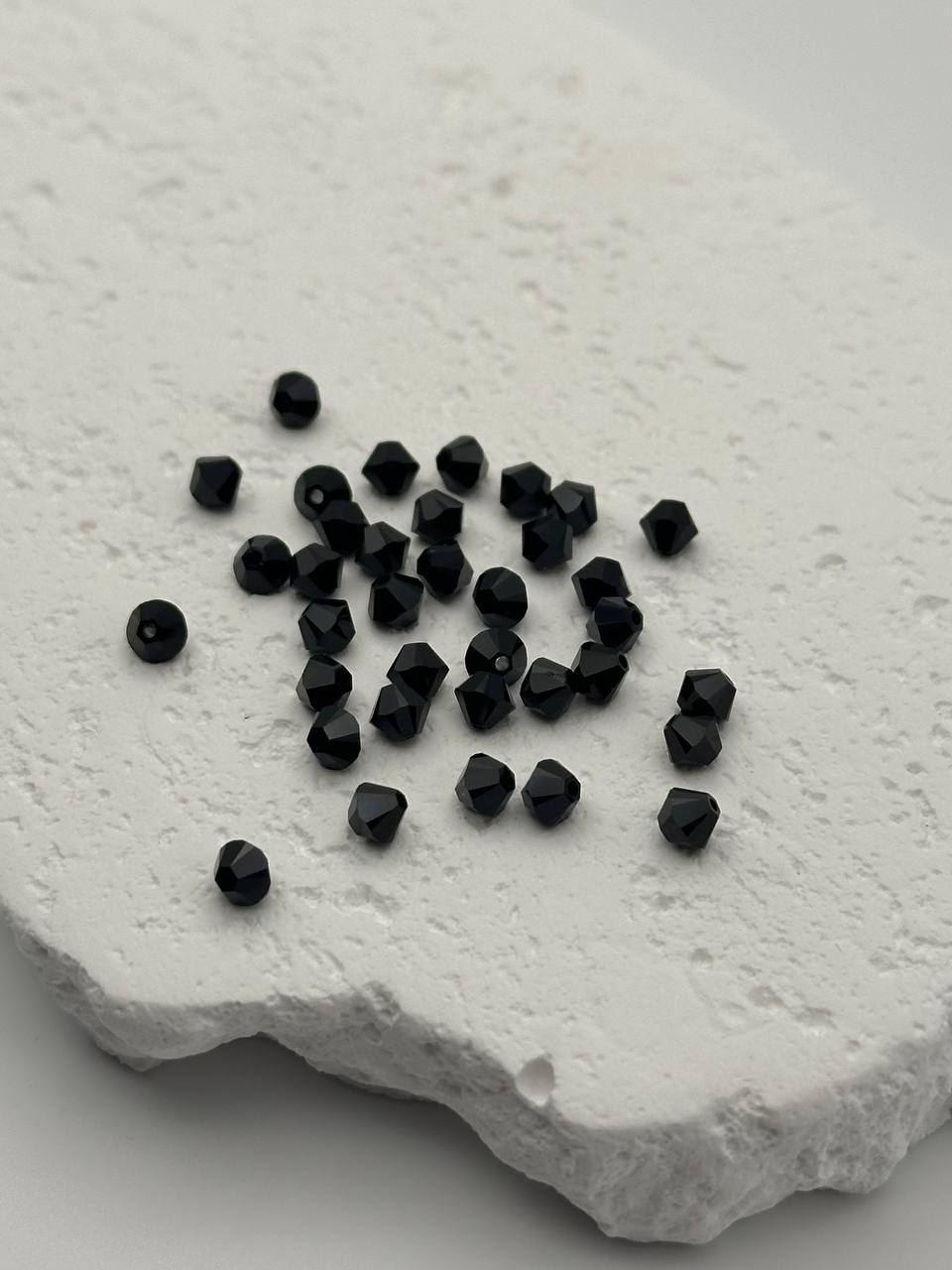 Black faceted bicone beads on a textured white surface