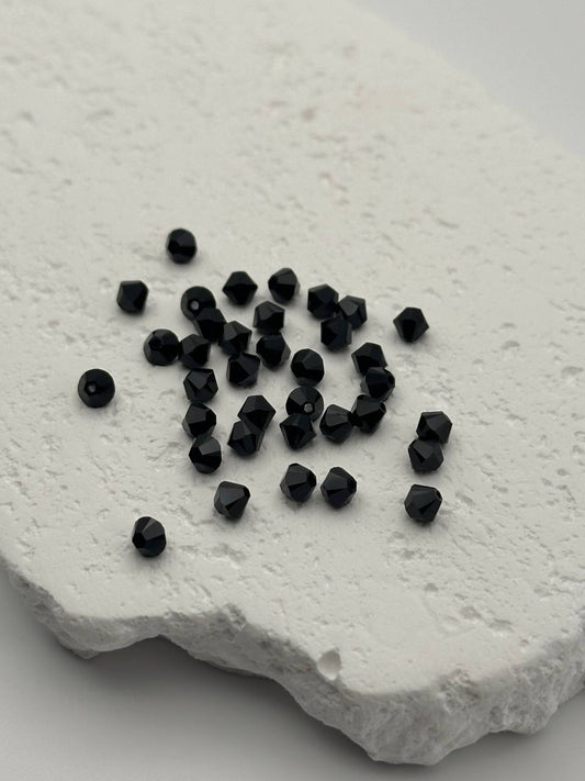Black faceted bicone beads on a textured white surface