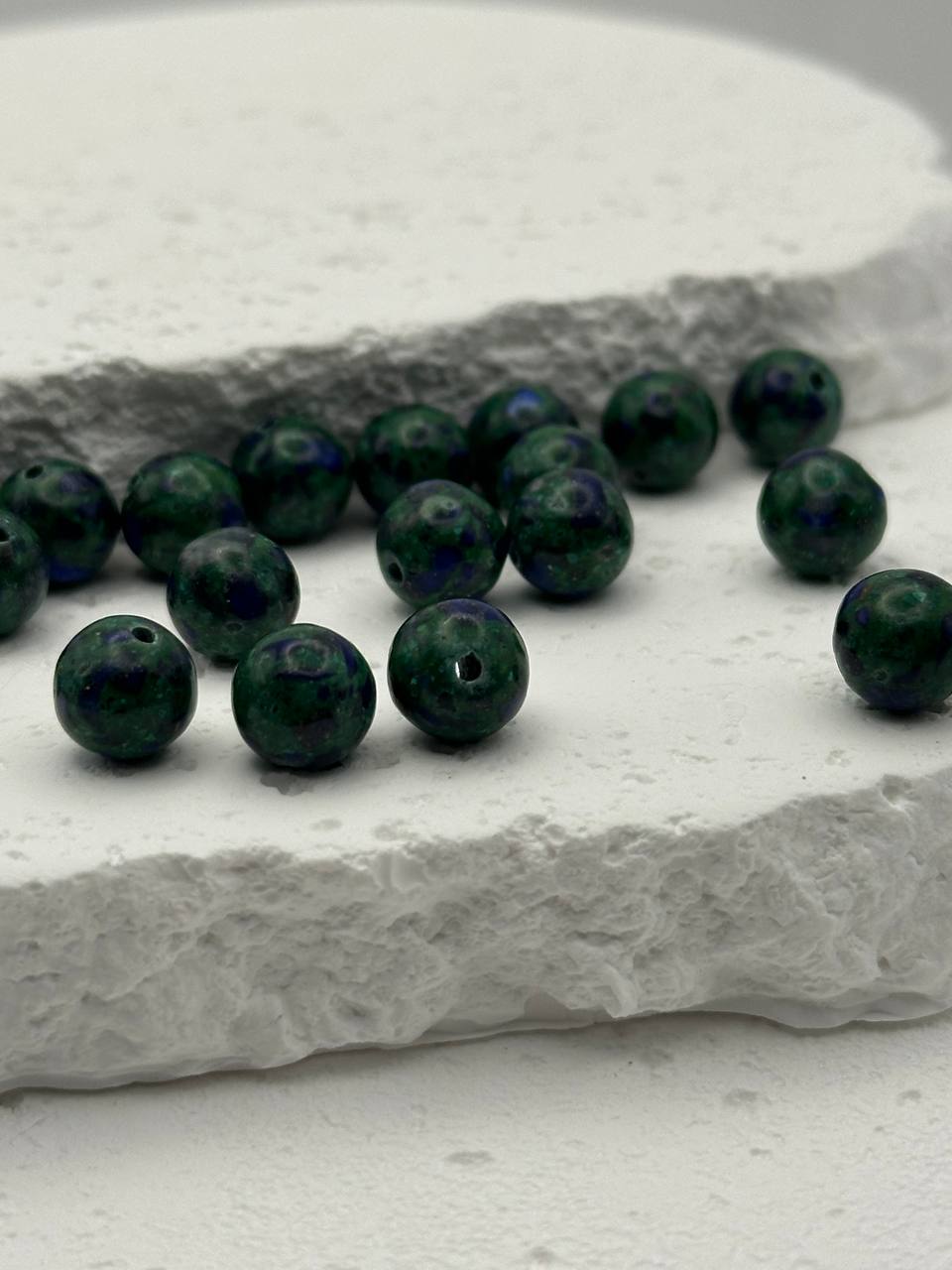 Green and purple beads on a textured white surface